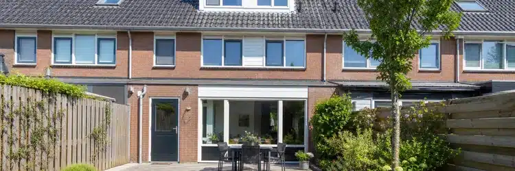 Witte kunststof dakkapel met plat dak aan de achterkant van een rijtjeswoning, vanuit de tuin gezien
